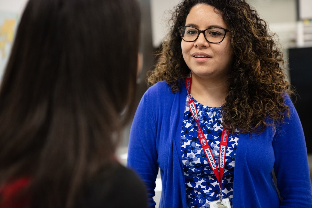 Female teacher in blue sweater talks to a student.