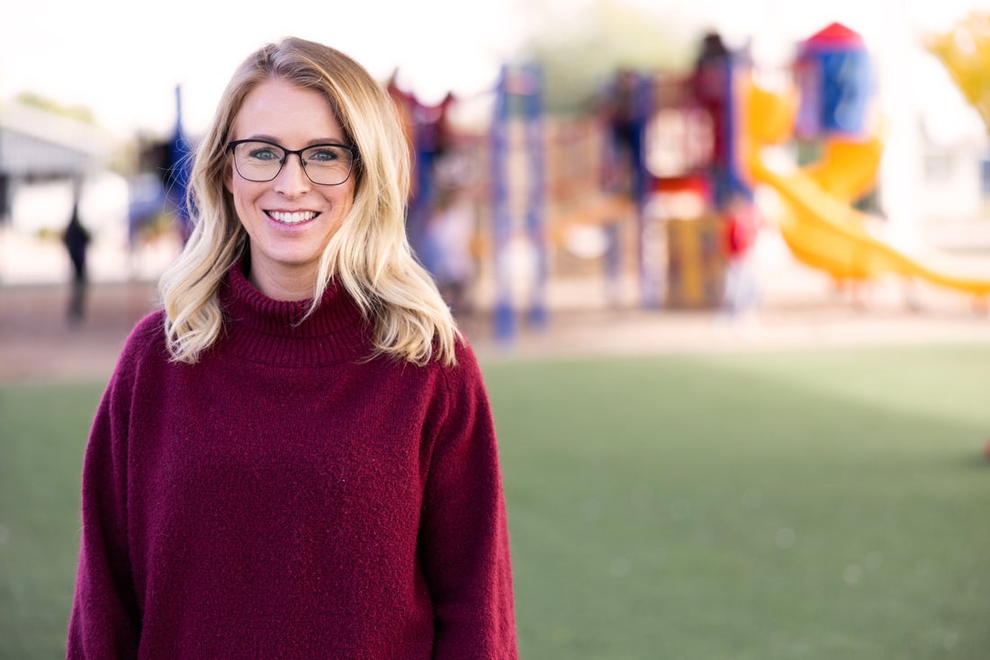 Young happy teacher standing in front of school play structure